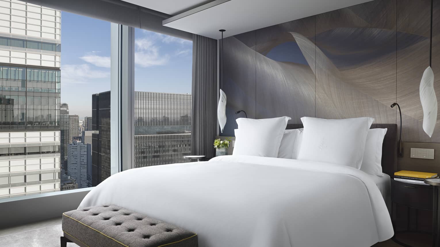 Luxurious bedroom with a king bed, upholstered bench and floor-to-ceiling windows with city views