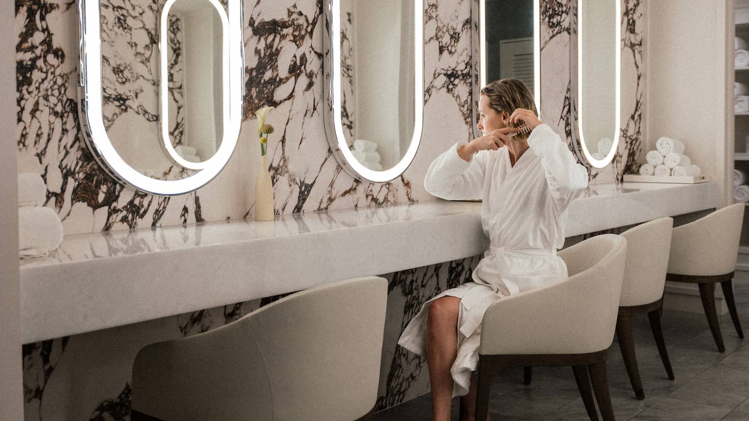 A person wearing a robe and sitting in front of a mirror and styling their hair