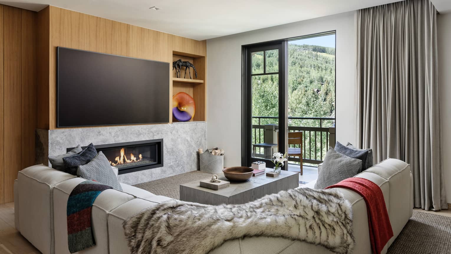 Living room with white sectional sofa, large TV, built-in fireplace and walk-out balcony at Four Seasons Residences Vail