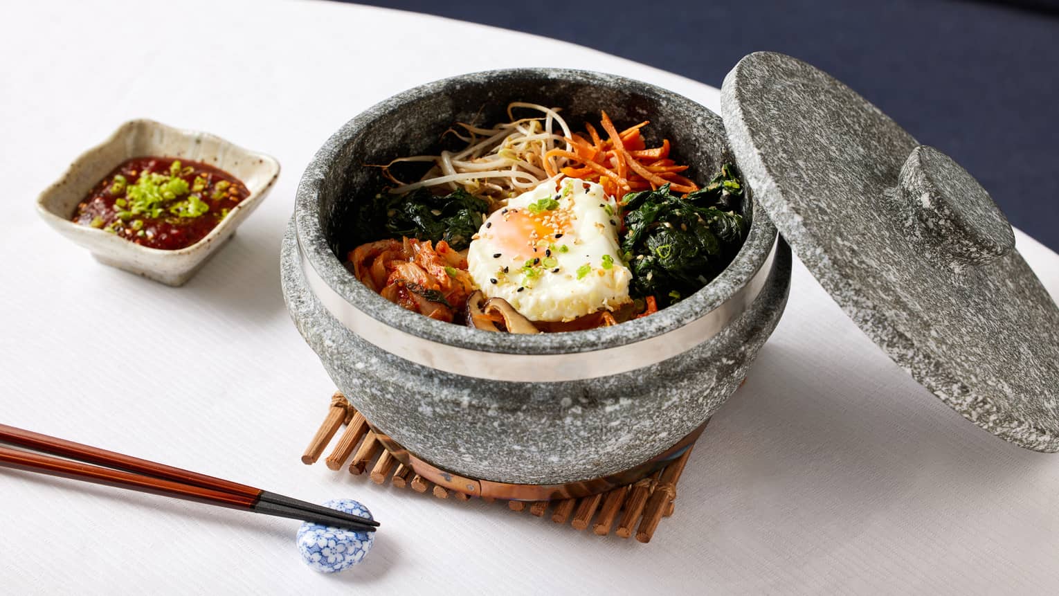 Kimchi bibimbap plated in a stone bowl with the lid ajar