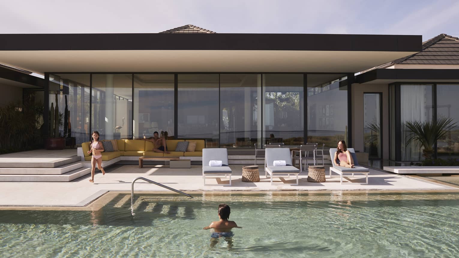 Kids playing in pool while adults lounge in chairs.