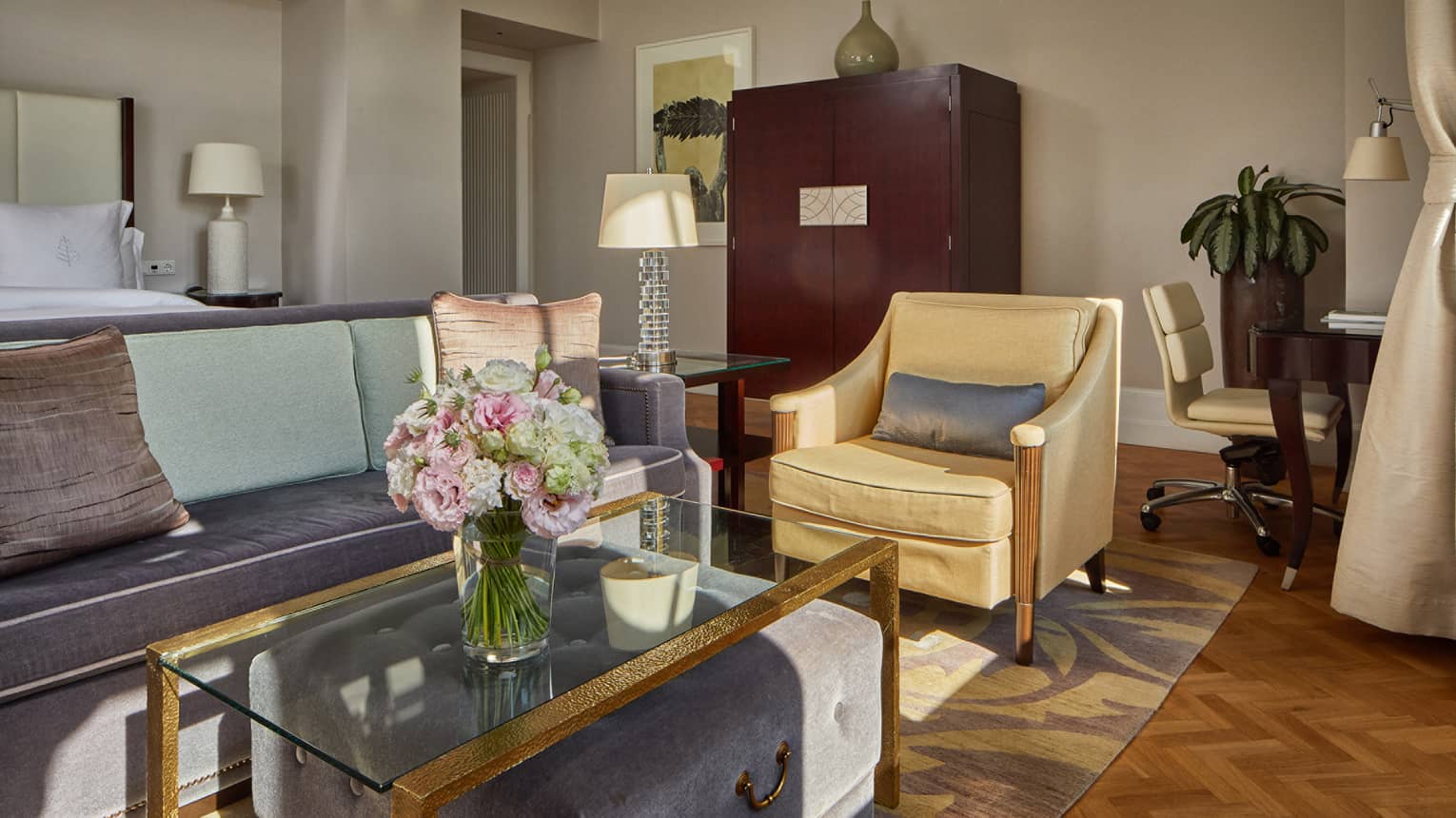 Elegant hotel suite with sofa, armchair, glass coffee table and floral arrangement