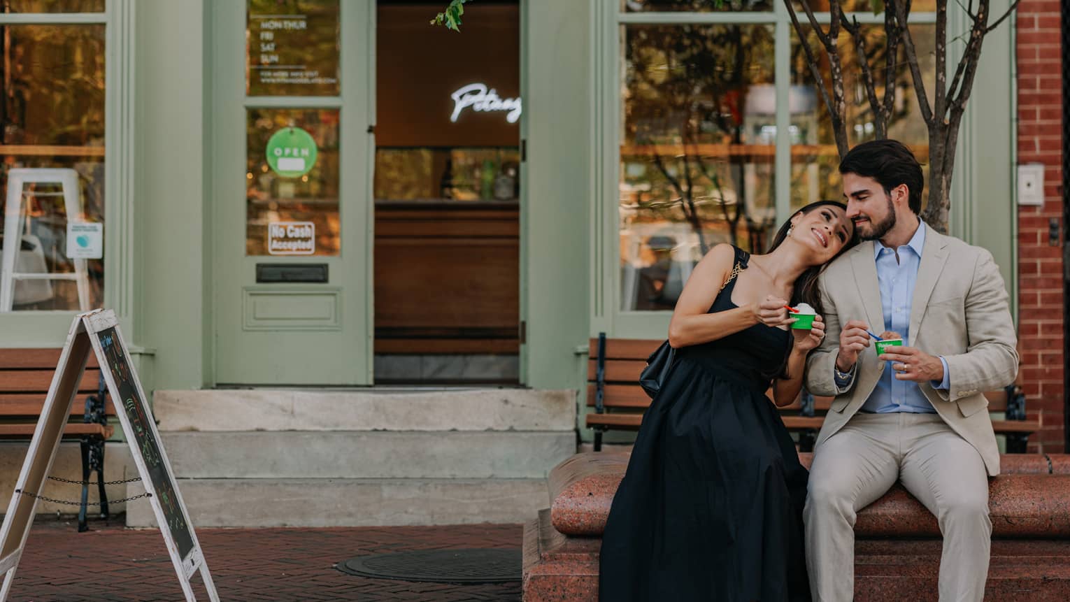 Two guests sitting together on a bench in front of a store and eating ice cream