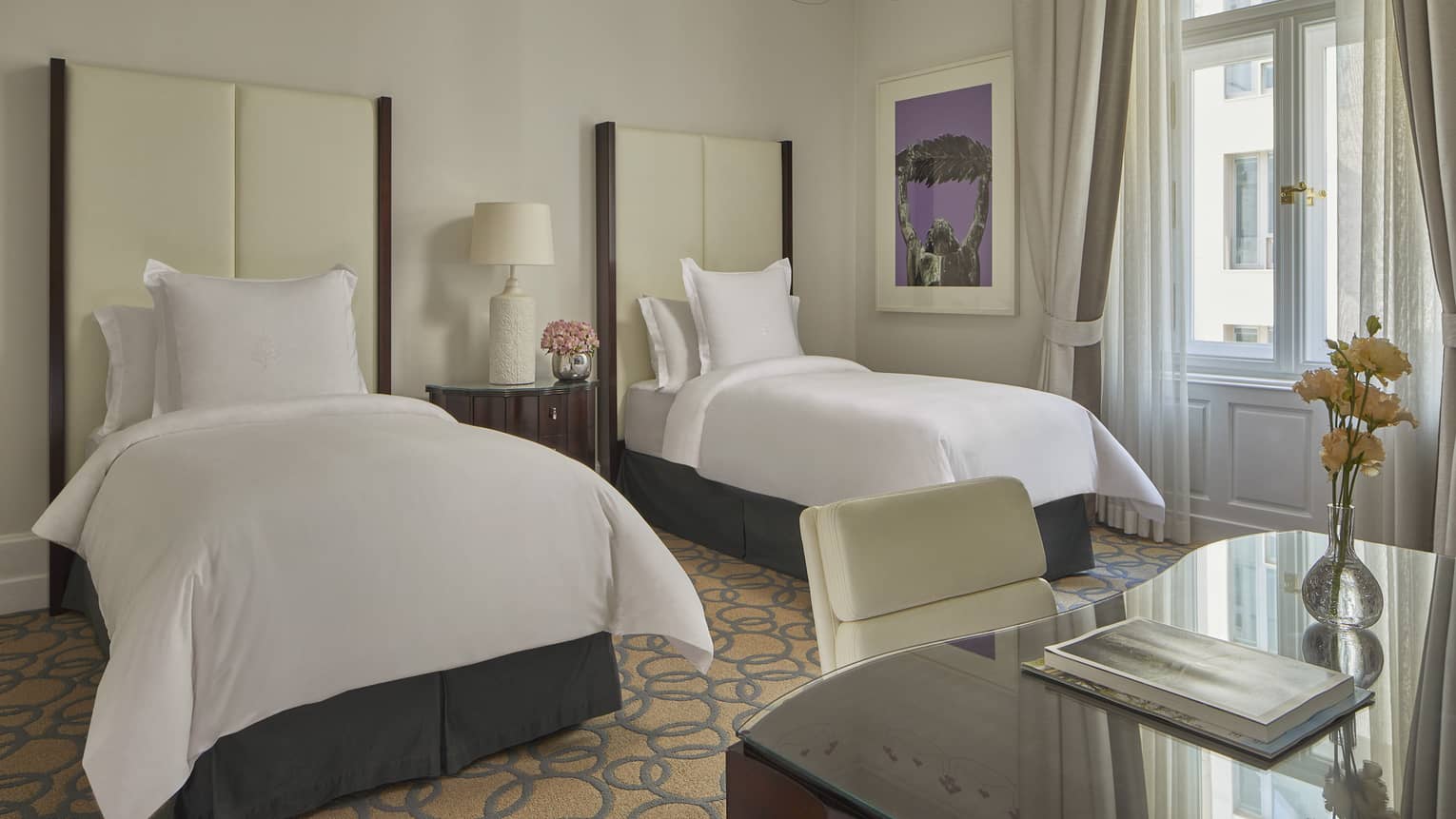 Elegant hotel room with two twin beds, a desk and a window with sheer curtains