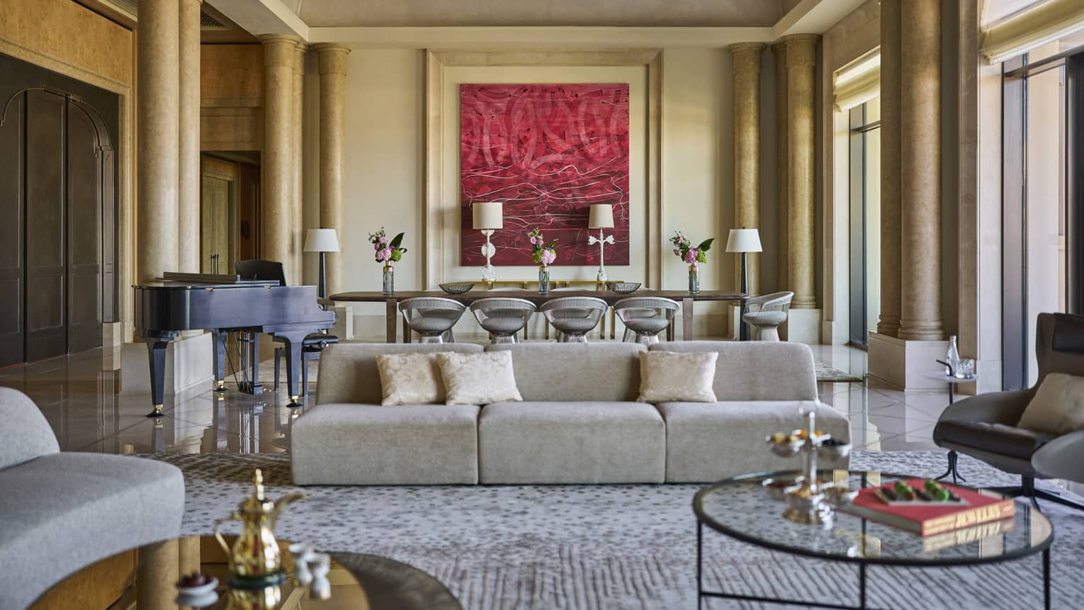 Grand hotel suite living room with pillars, a modern sofa and a large dining table set next to red artwork