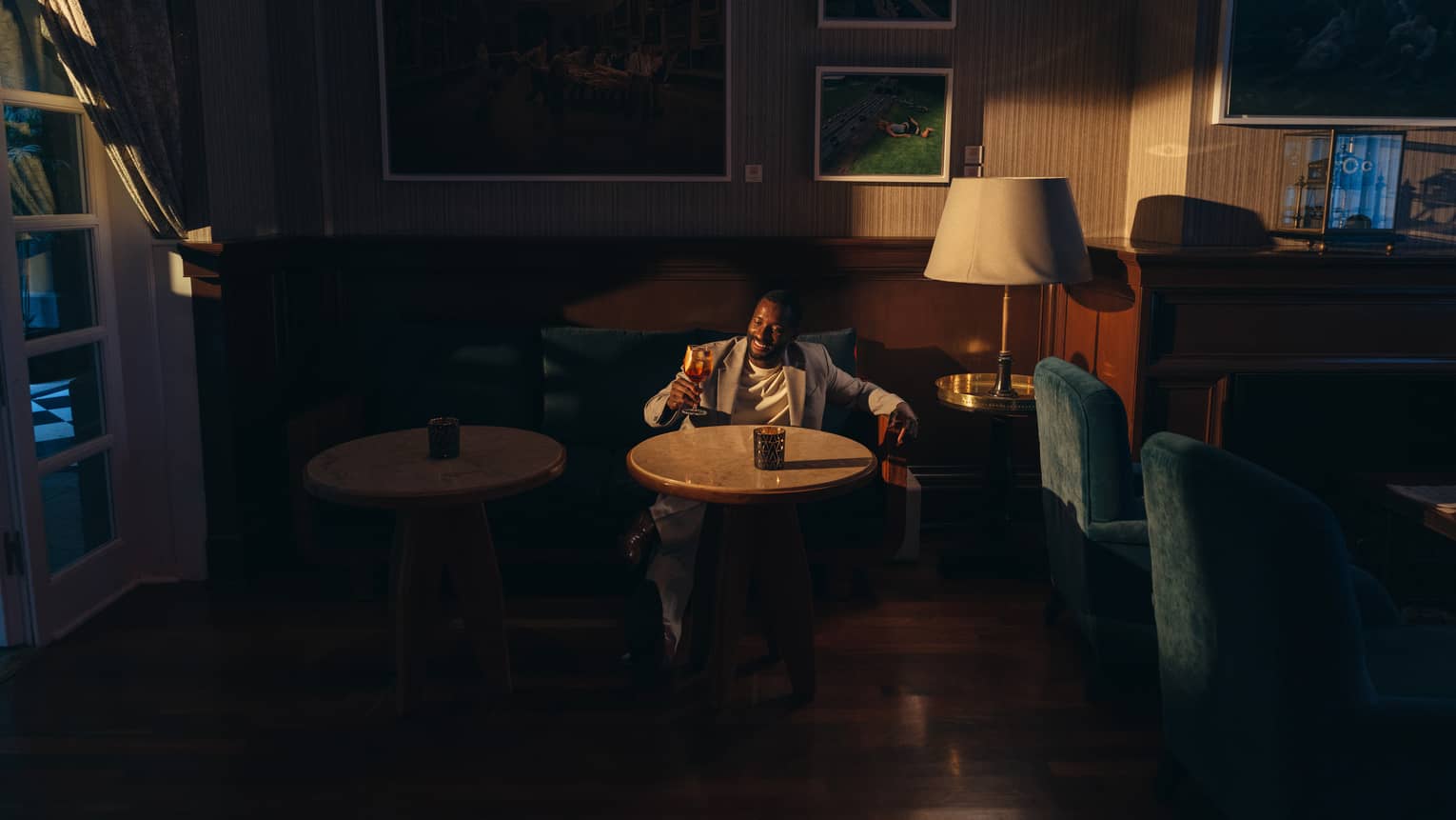 A person holding a drink sits at a table in a bar