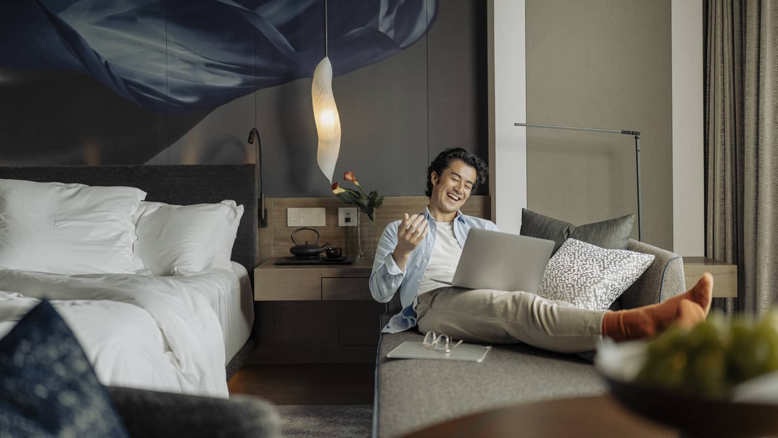 Laughing man lounges on sofa with laptop in his guest room