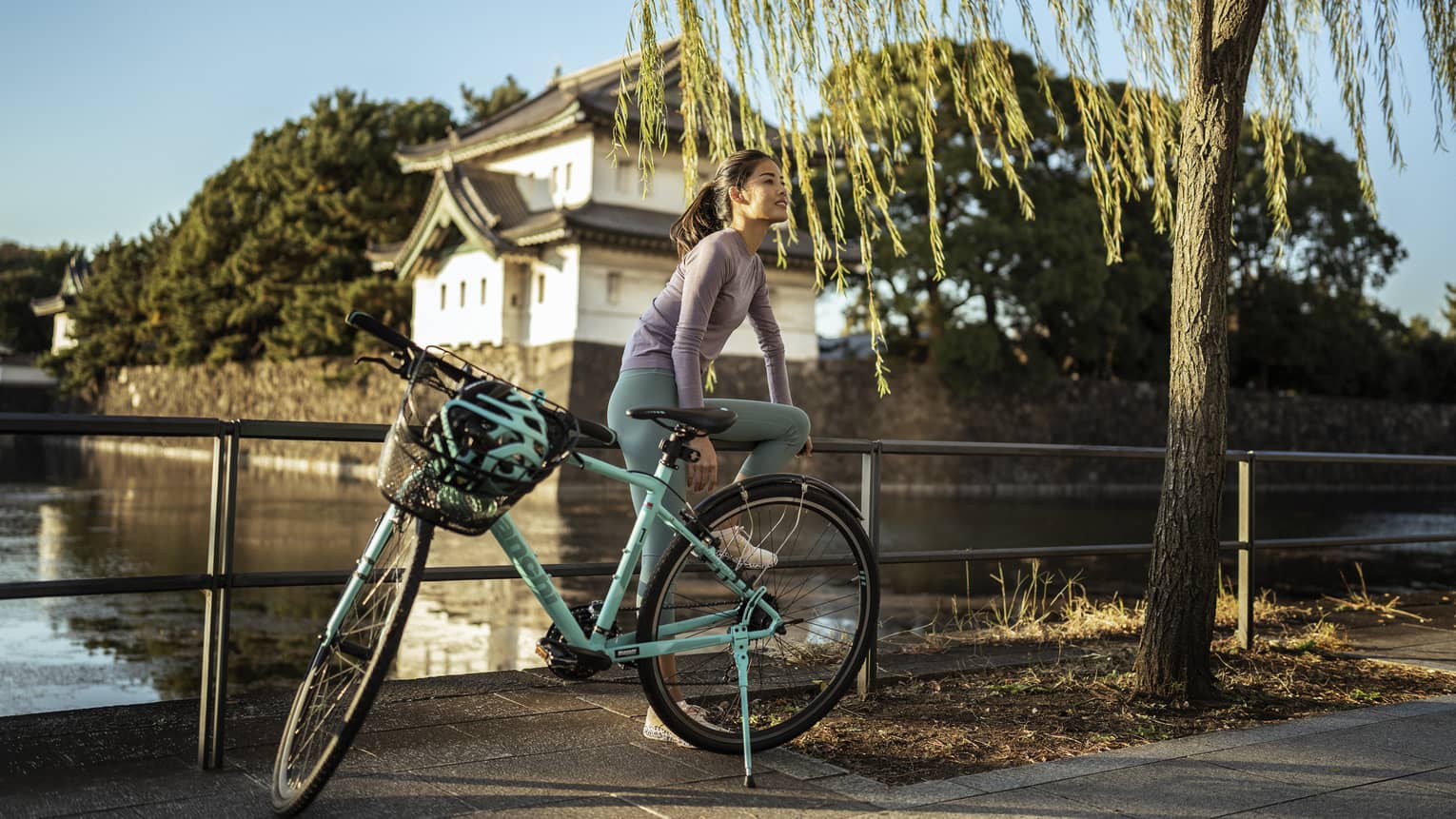 Woman sits on rail of bridge with teal cruiser bike in front of Japanese pagoda
