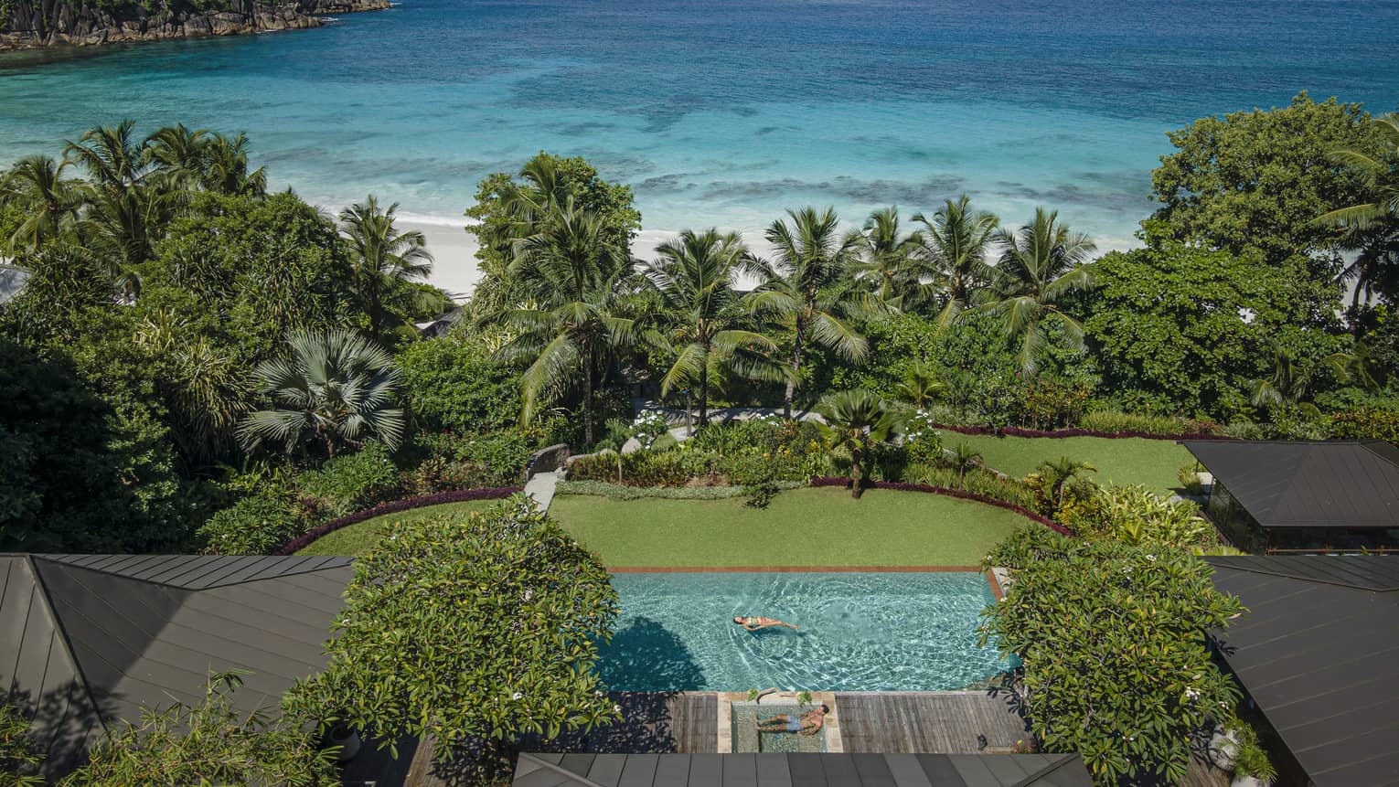 Private pool beside green lawn leading to tropical foliage and a white-sand beach and ocean beyond