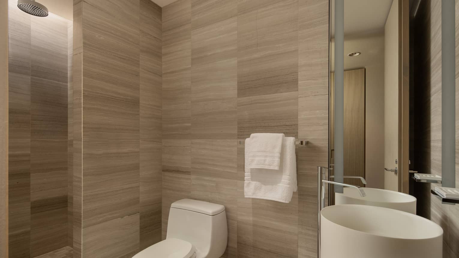 Hotel suite bathroom with a toilet, round sink, two towels on a rack and rain shower head