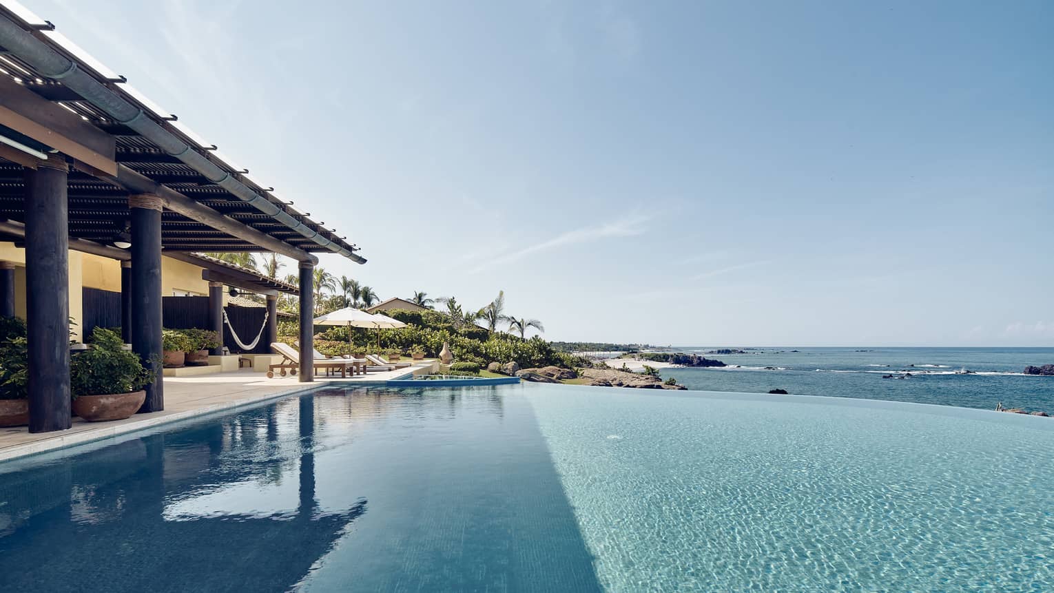 View over infinity swimming pool looking over ocean, covered patio at side