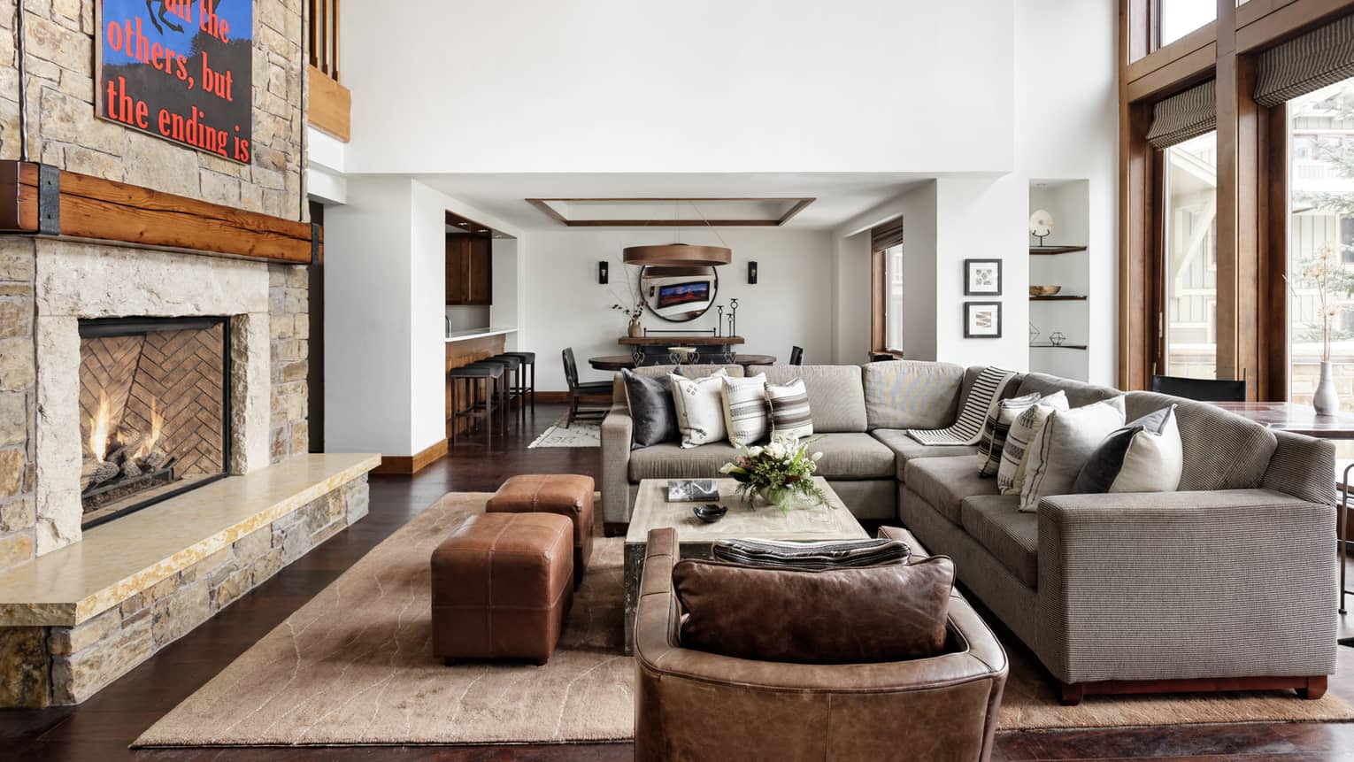 Luxury living room with a stone fireplace, statement art piece, sectional sofa, leather armchair and ottomans, and views of a dining area and bar seating