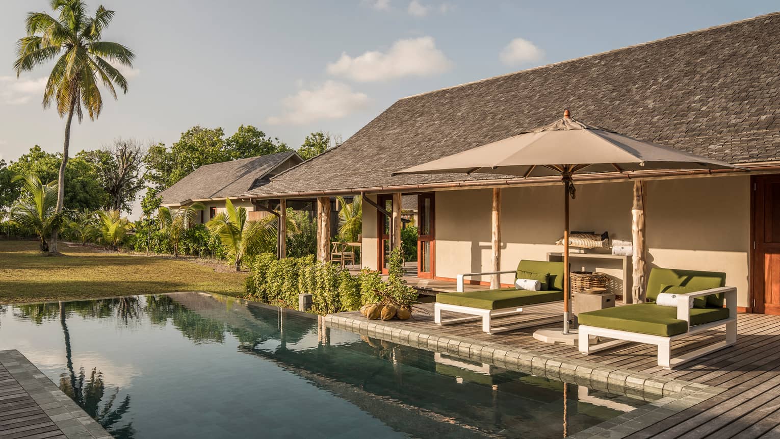 Palm tree reflecting on plunge pool under bungalow small patio with two lounge chairs, umbrella