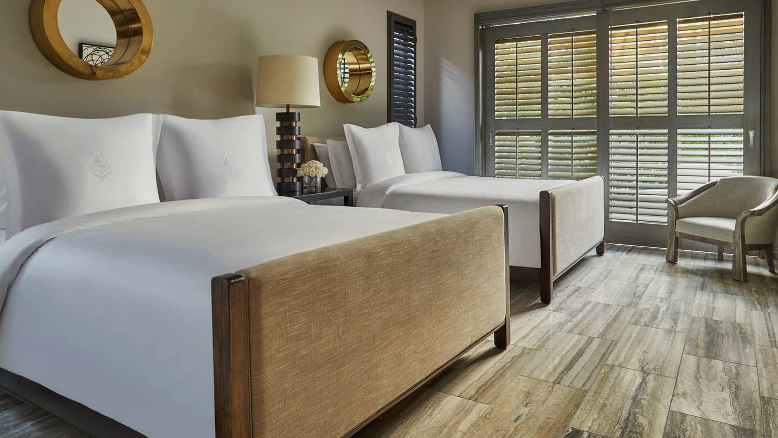 Two double beds in a serene guest room with wood floors, neutral tones and large shuttered windows