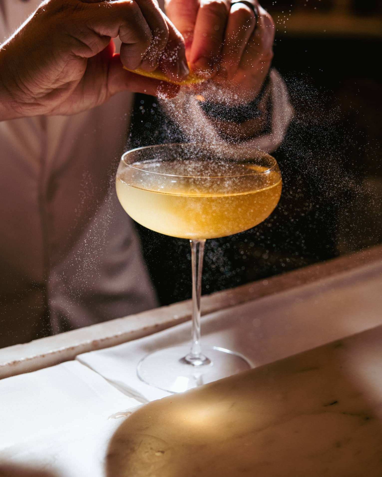 A cocktail being garnished with an orange spritz.