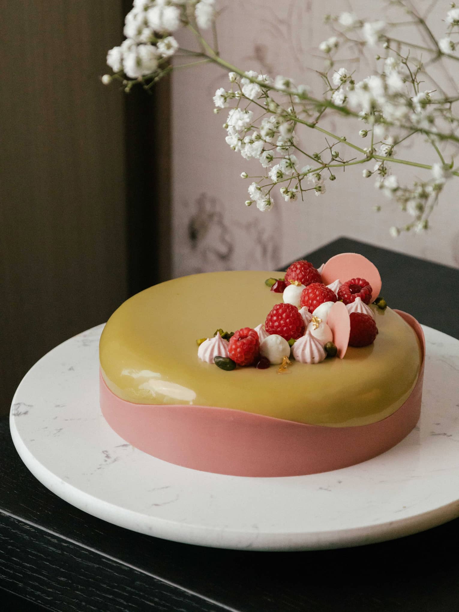 Pink and yellow cake on plate with spray of flowers in background