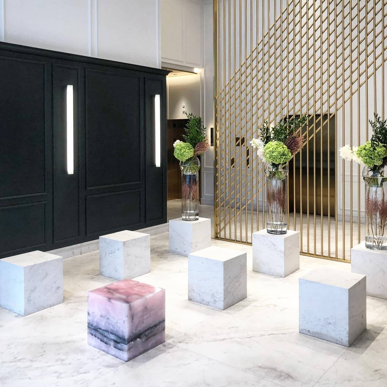 The lobby of the Four Seasons Hotel, Montreal, with large decorative marble blocks, marble flooring, green floral arrangements, and a gold partition