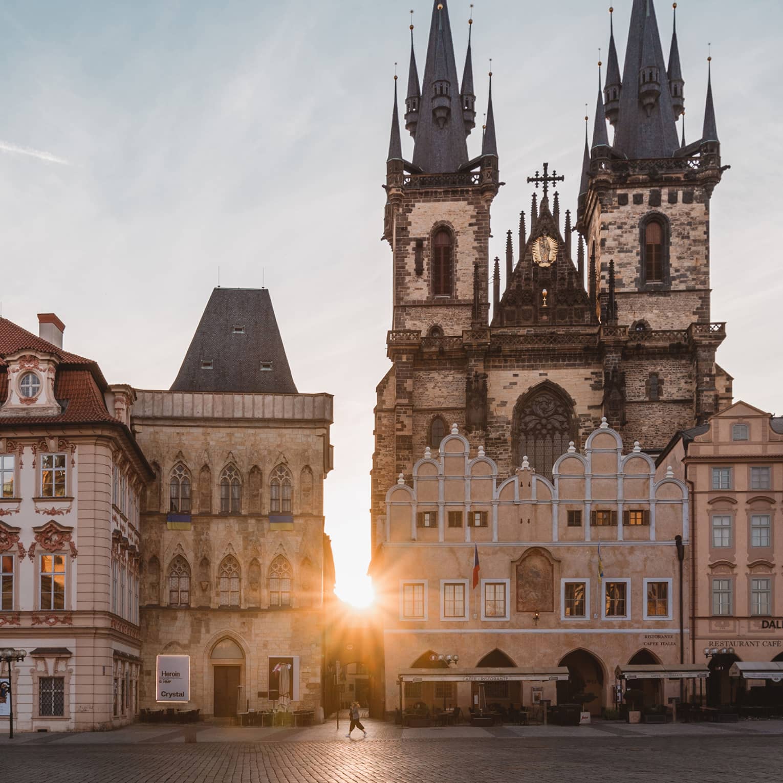 Sunset bursts through a medieval building with an intricate exterior and a formidable Gothic church with soaring spires.