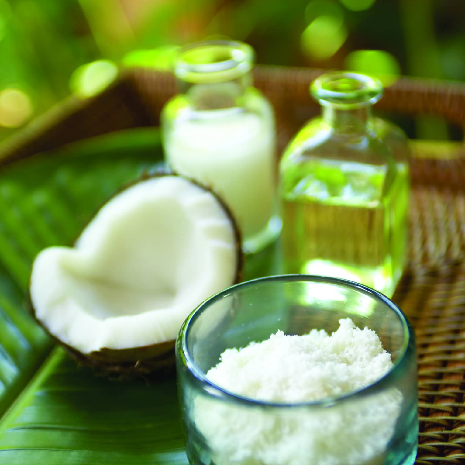 Half of a cracked coconut shell next to small glass bowl with coconut flakes