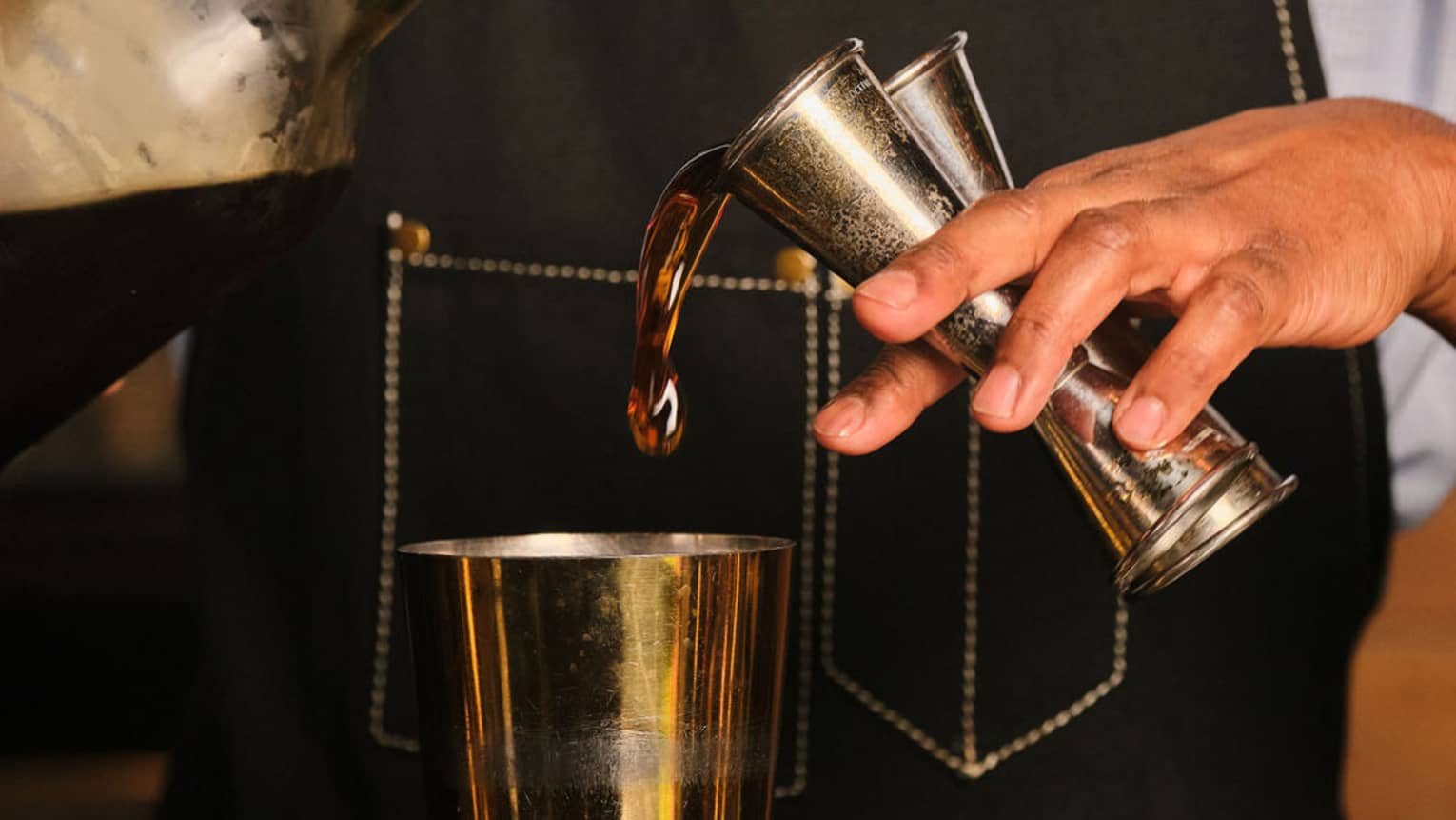 A bartender pours liquid from two jiggers into a cocktail shaker