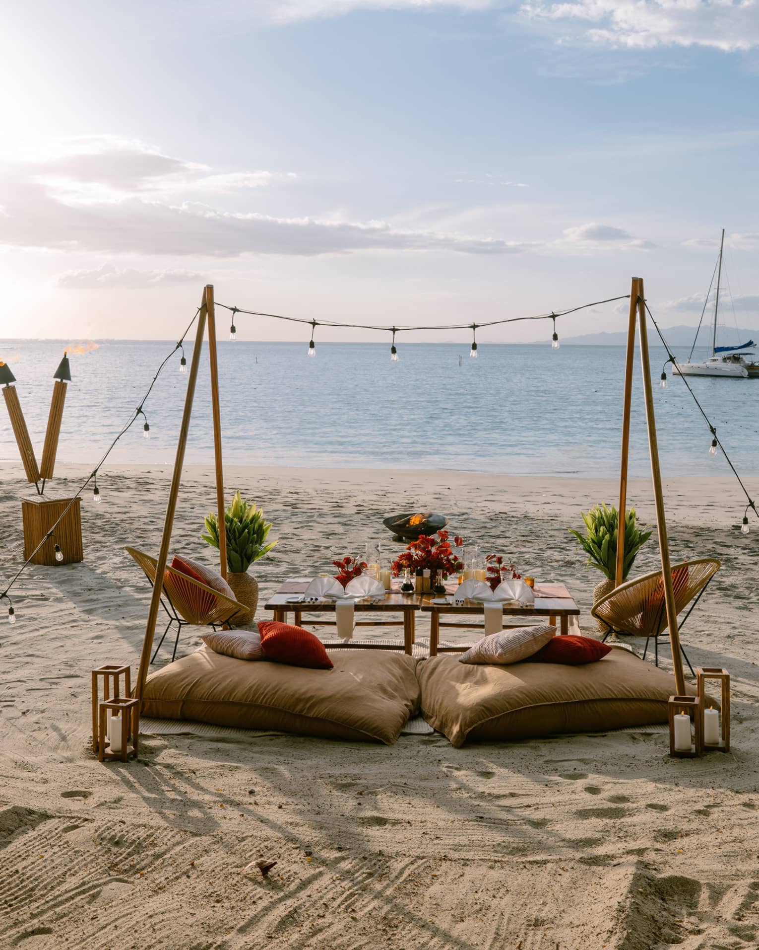 Private dining set up on a beach with two cusions, a table, string lights and rustic decorations