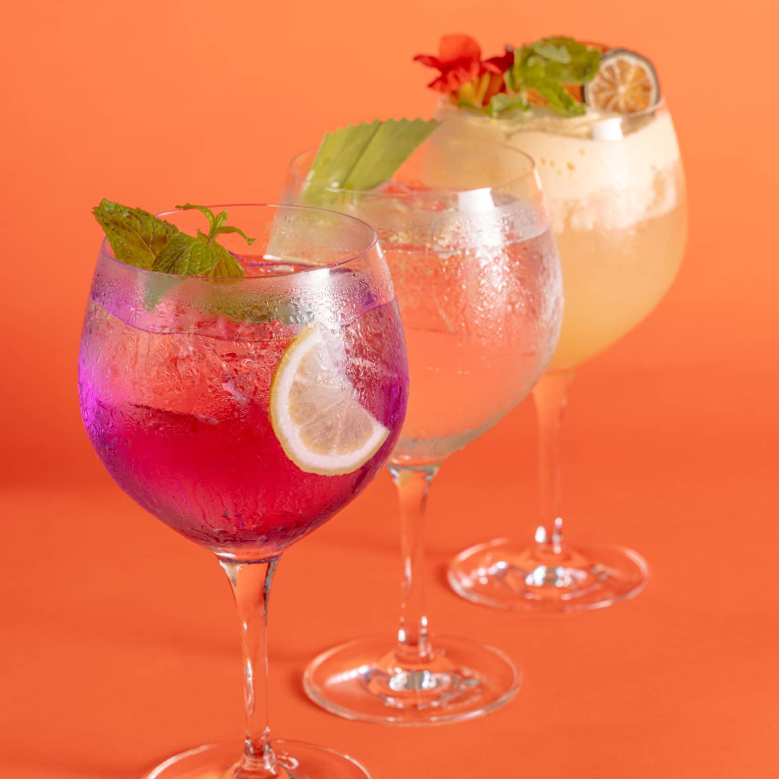 Three different cocktails in tall, stemmed glasses on orange background