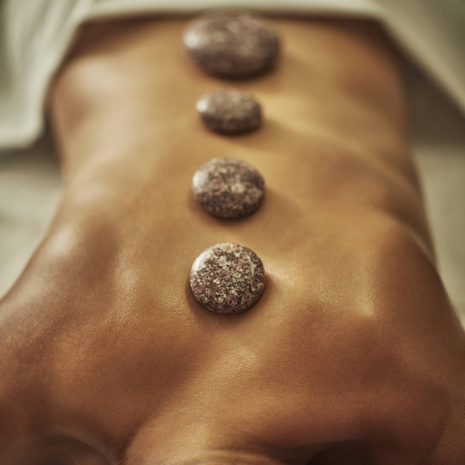 A woman lies on a spa table with four hot stones laid on her back