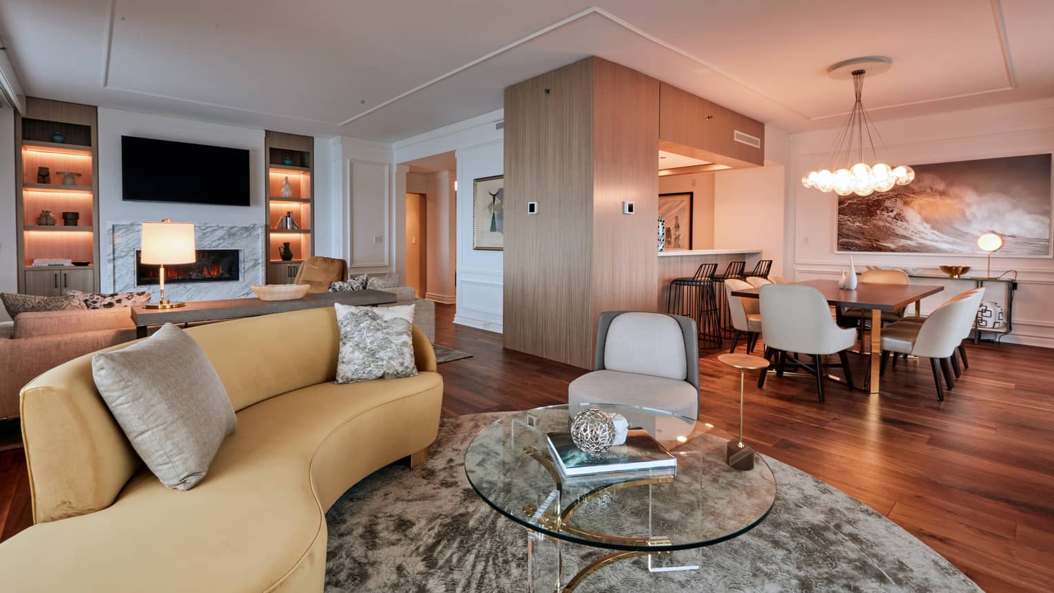 Living room with mustard-yellow curved sofa, glass round coffee table, opening to dining room