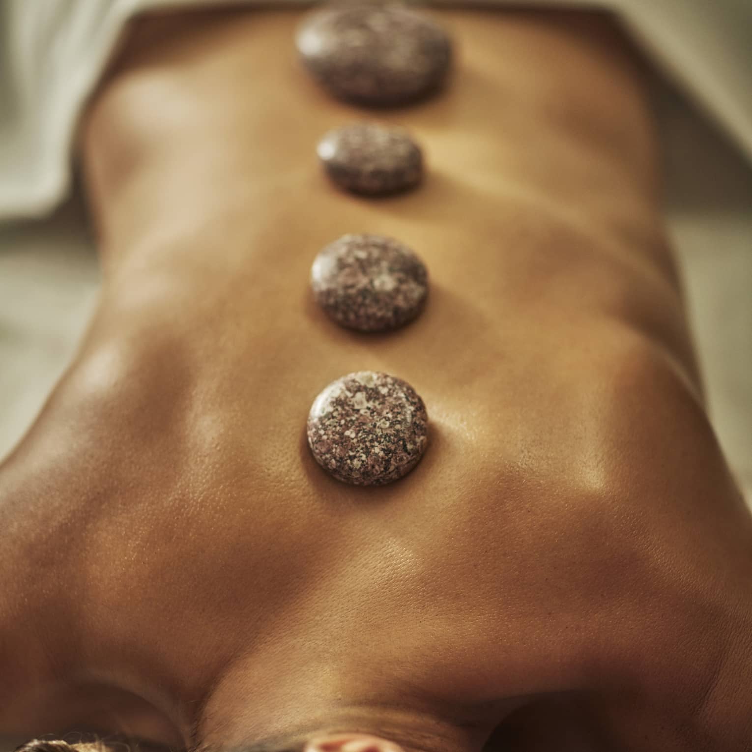 A woman lies on a spa table with four hot stones laid on her back
