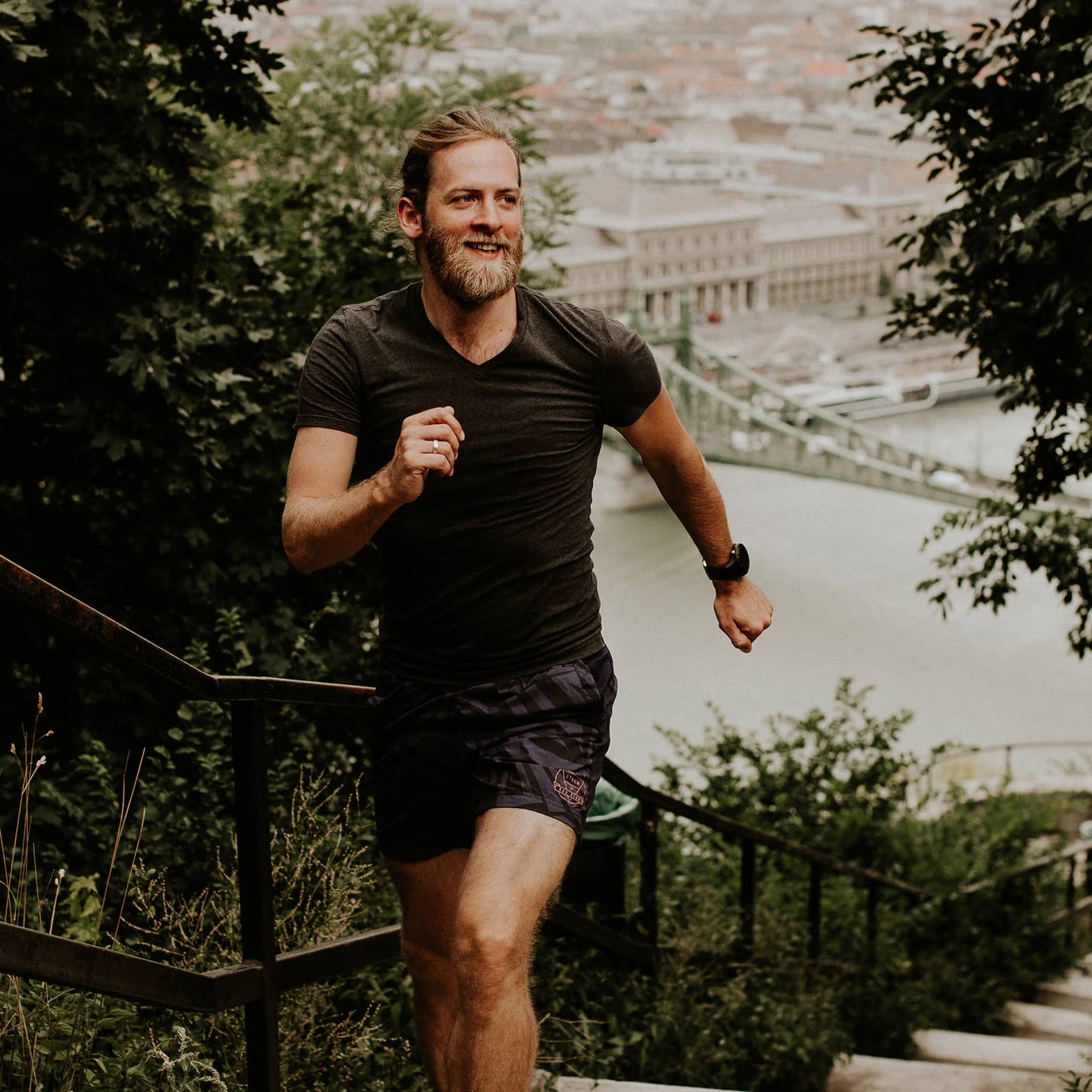 Front view of a runner on a hilltop staircase in morning light, a backdrop of old-world architecture along the harbour below.