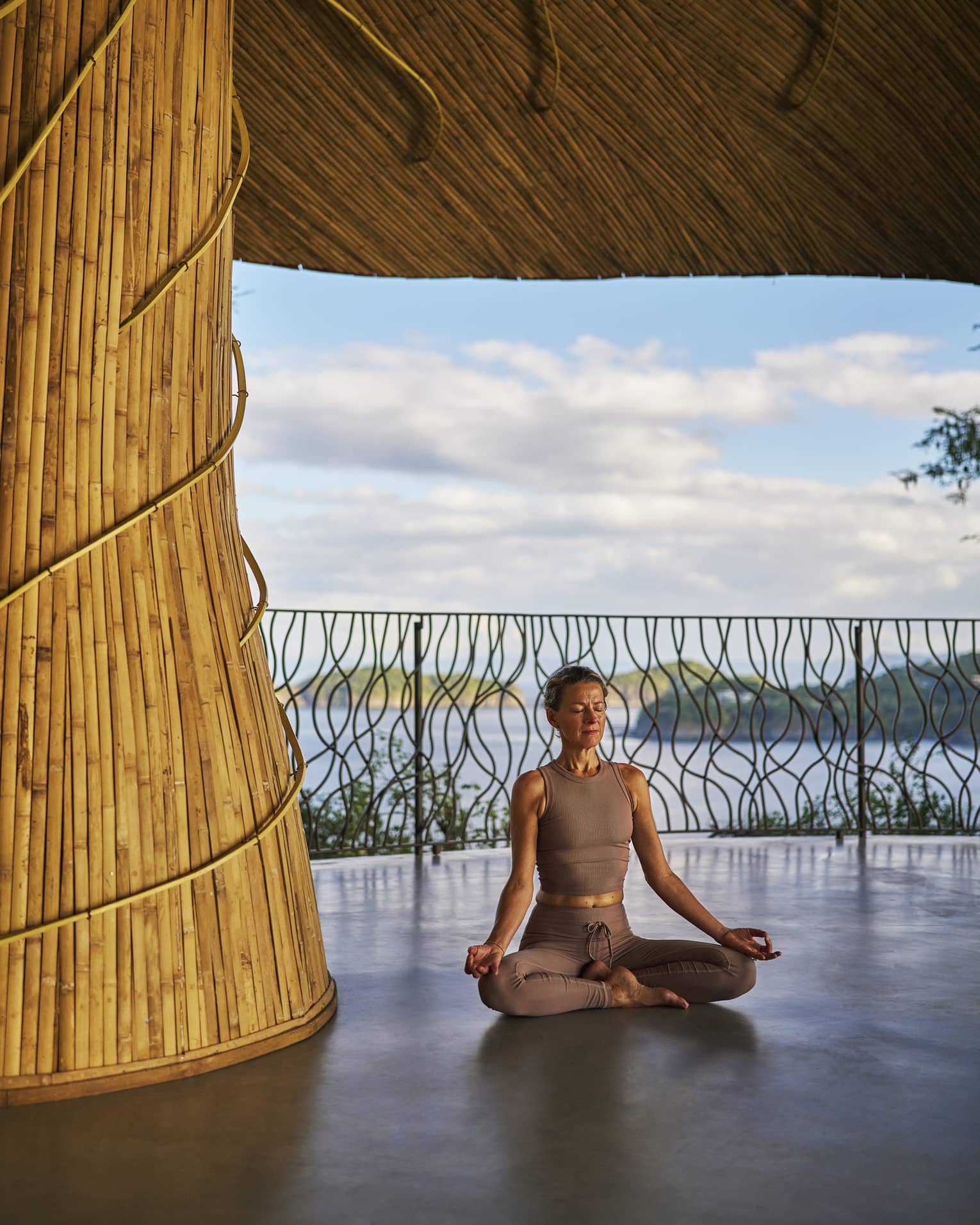 Person sits cross-legged inside an open-air wellness shala with the sea in the background