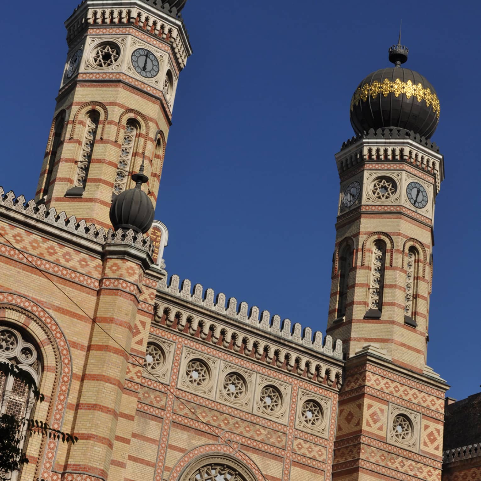A majestic synagogue featuring two towers and arrays of carvings encircling shapes resembling the hexagonal star of David.