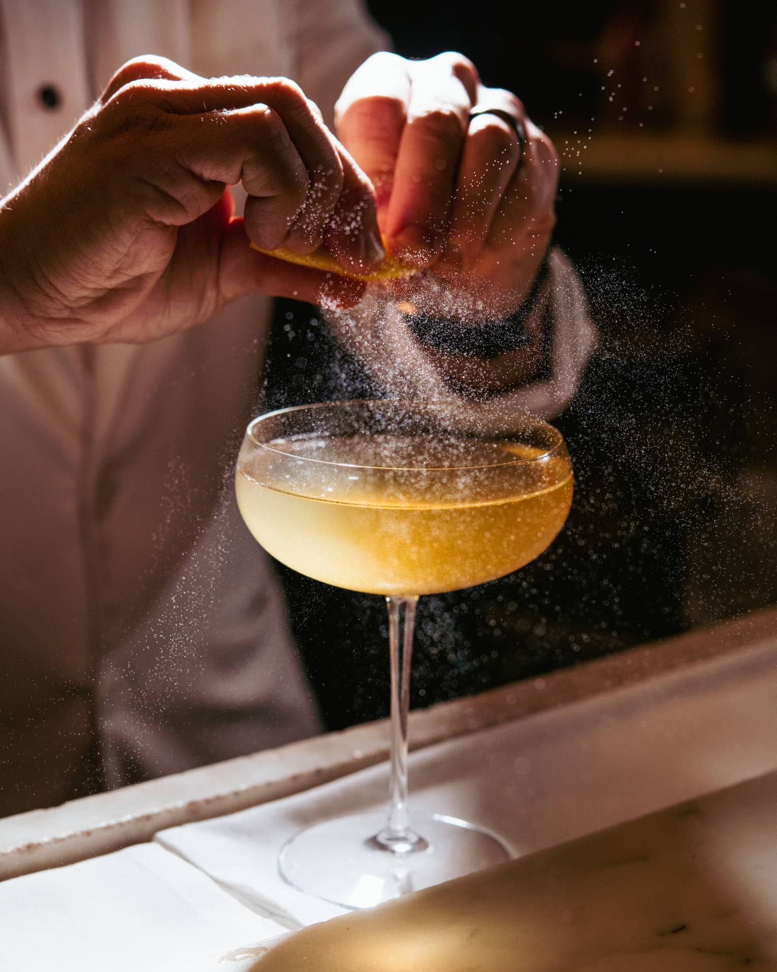 A cocktail being garnished with an orange spritz.