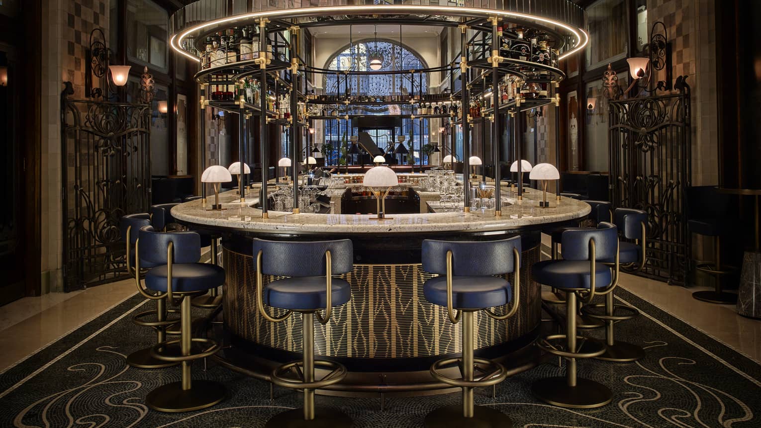 Elegant round bar with blue chairs and overhead glass rack in a grand interior space