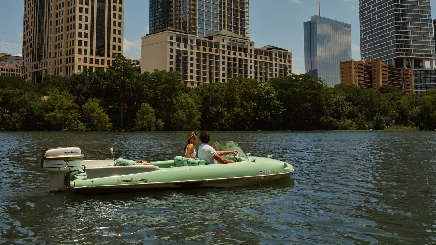 Two guests on a boat in the water with city buildings in the background