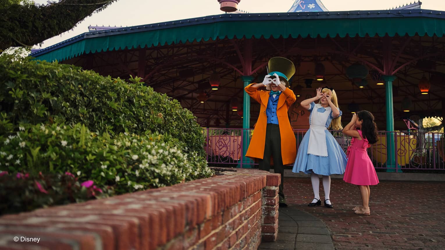 People dressed as Alice in Wonderland and the Mad Hatter stand with a child wearing a bright pink dress