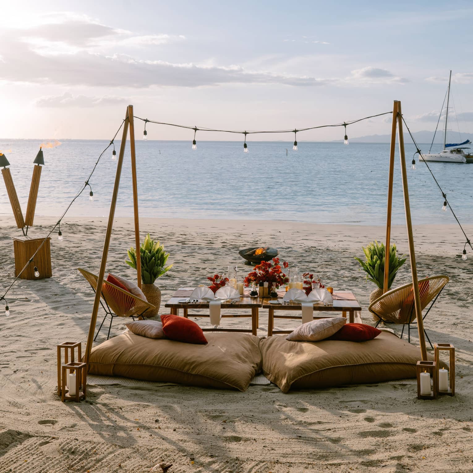 Private dining set up on a beach with two cusions, a table, string lights and rustic decorations