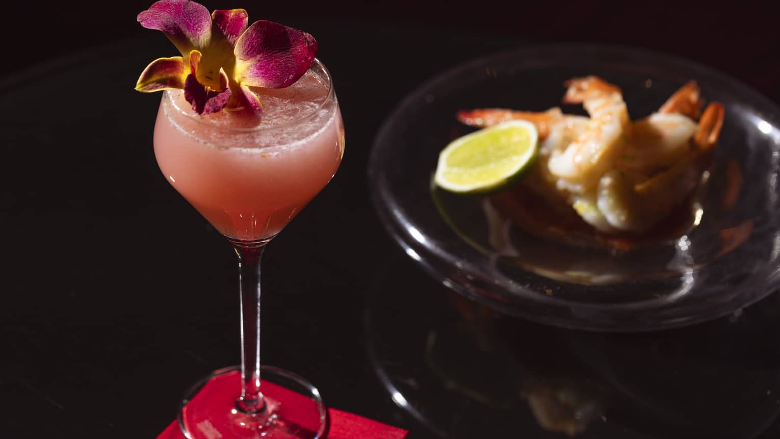 A cocktail garnished with a flower rests on a napkin