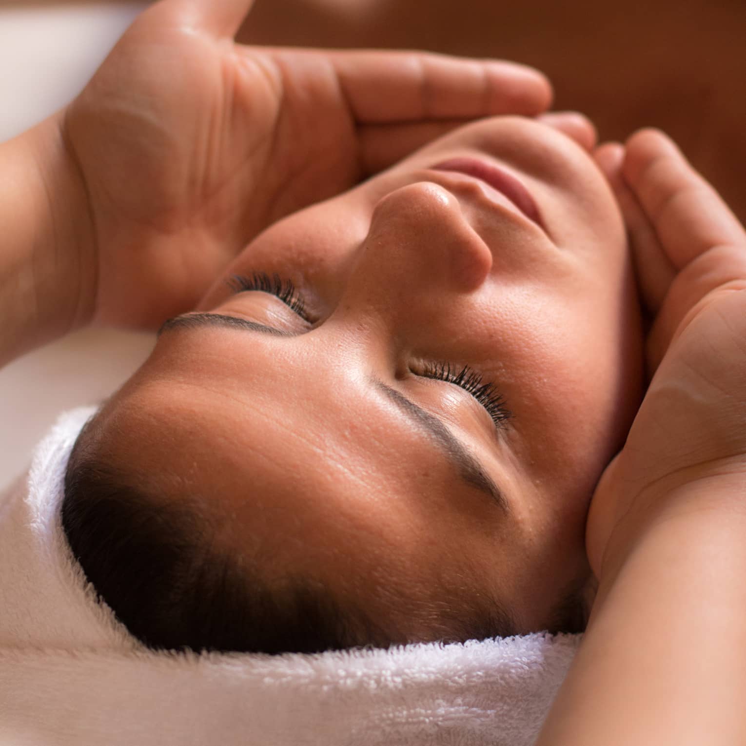 Close-up of woman with eyes closed facing up as hands cup her face and chin