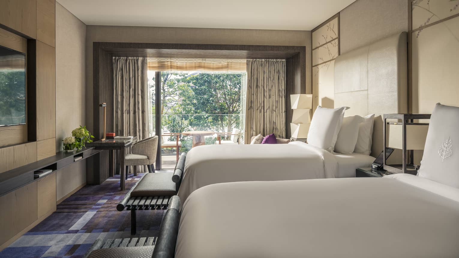 Hotel room with two beds, a work desk and a private balcony with outdoor seating and garden view