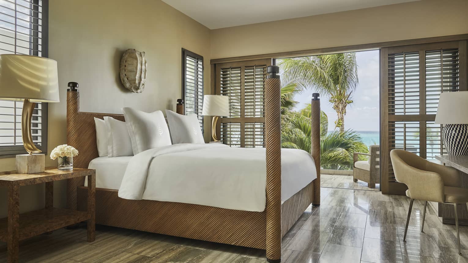 Bright bedroom with four-poster bed, wood accents and balcony view of palm trees and ocean.
