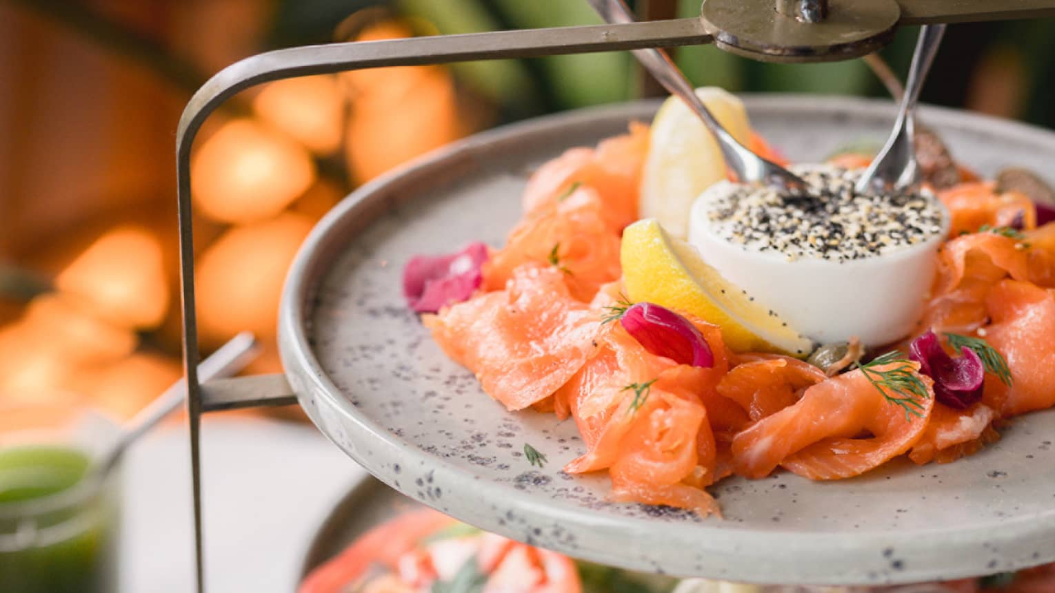 A three-tiered platter with salmon, tomatoes, a poached egg and croissants filling the levels.