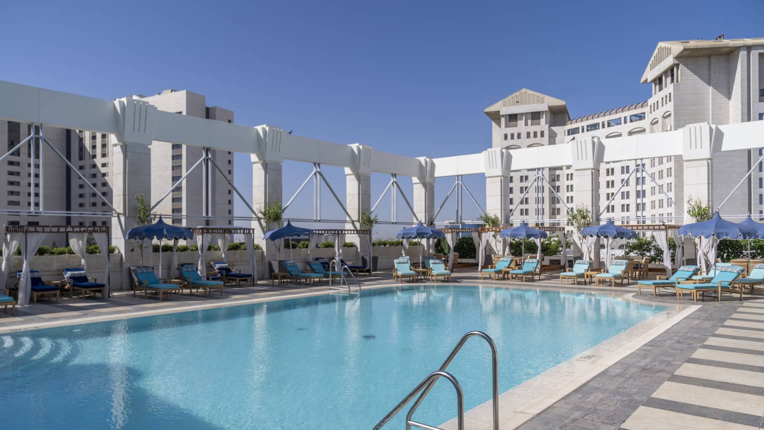 Outdoor pool surrounded by teal lounge chairs and white columns
