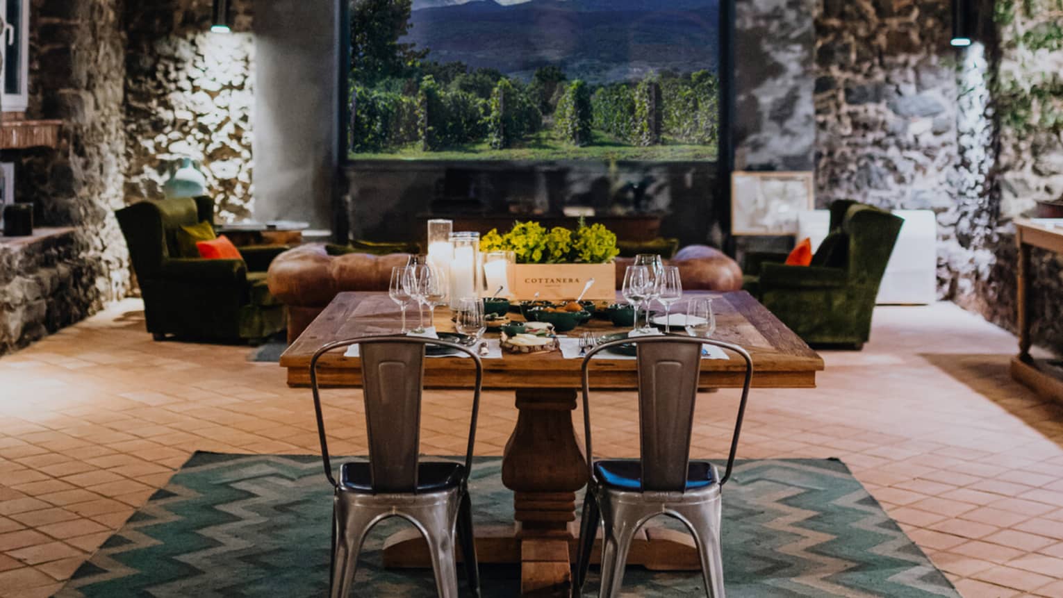 A wooden dining table set with floral arrangements and glassware, in a room with a window overlooking mountains and a vineyard