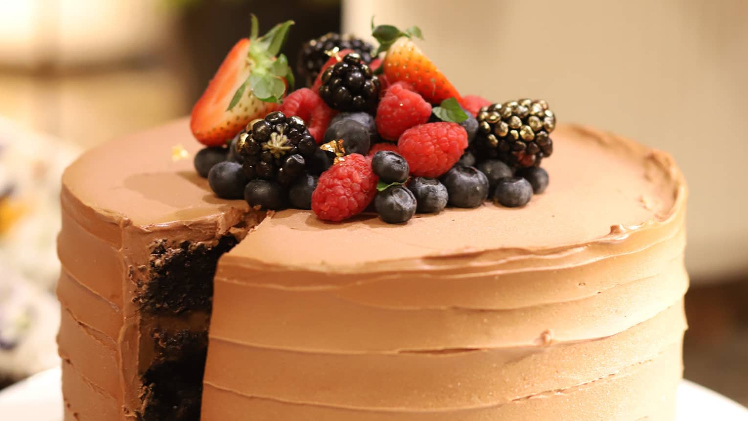 Round chocolate cake with chocolate frosting topped with fresh strawberries, blueberries, blackberries and raspberries