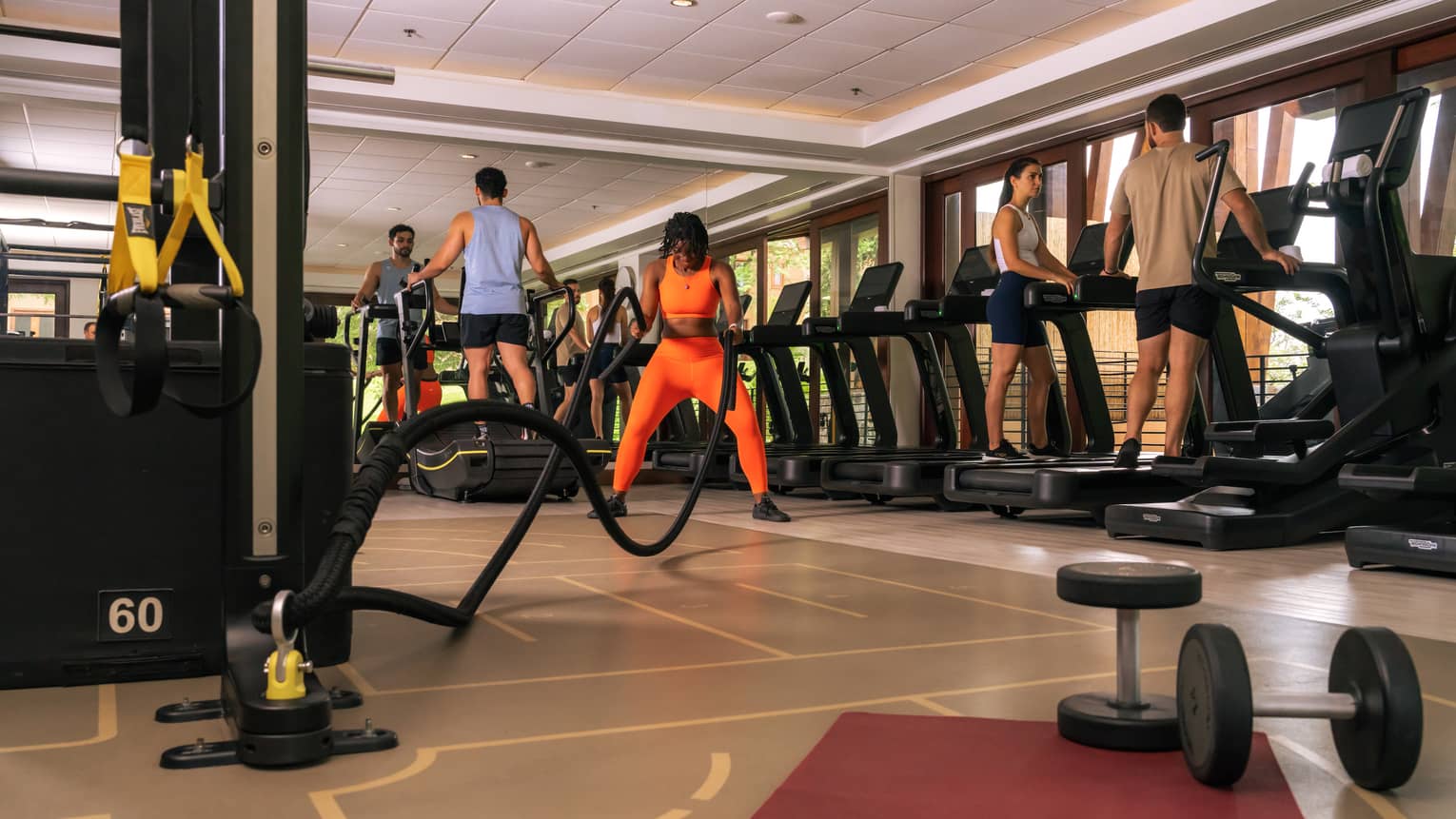 Five people workout in a resort fitness centre that features a row of treadmills and a variety of strength equipment