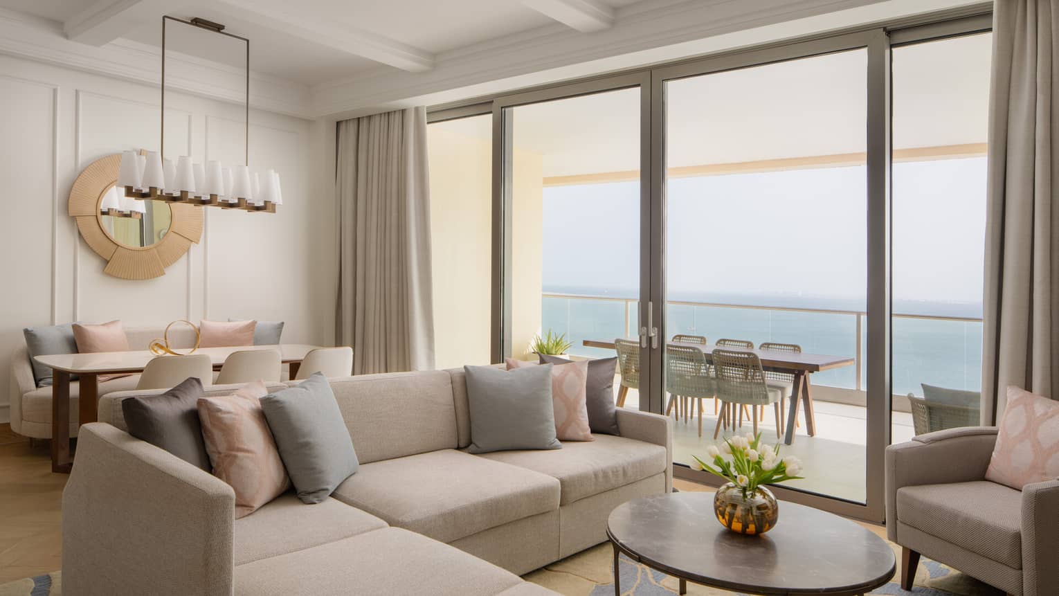 Contemporary living and dining area with neutral tones, a sectional sofa and large glass doors opening to a balcony with ocean views.,Contemporary living and dining area with neutral tones, a sectional sofa, and large glass doors opening to a balcony with ocean views.
