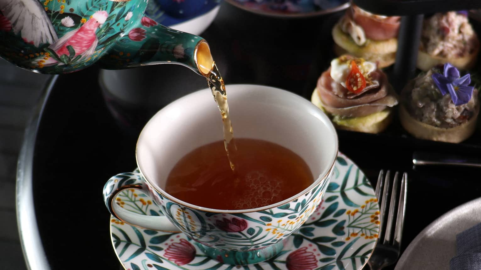 Tea being poured into tea cup with a floral design.