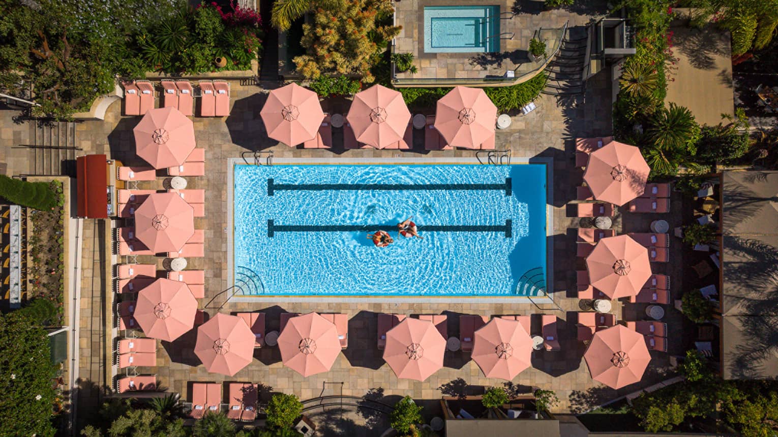 Aerial view of luxury hotel pool surrounded by pink umbrellas and lounge chairs