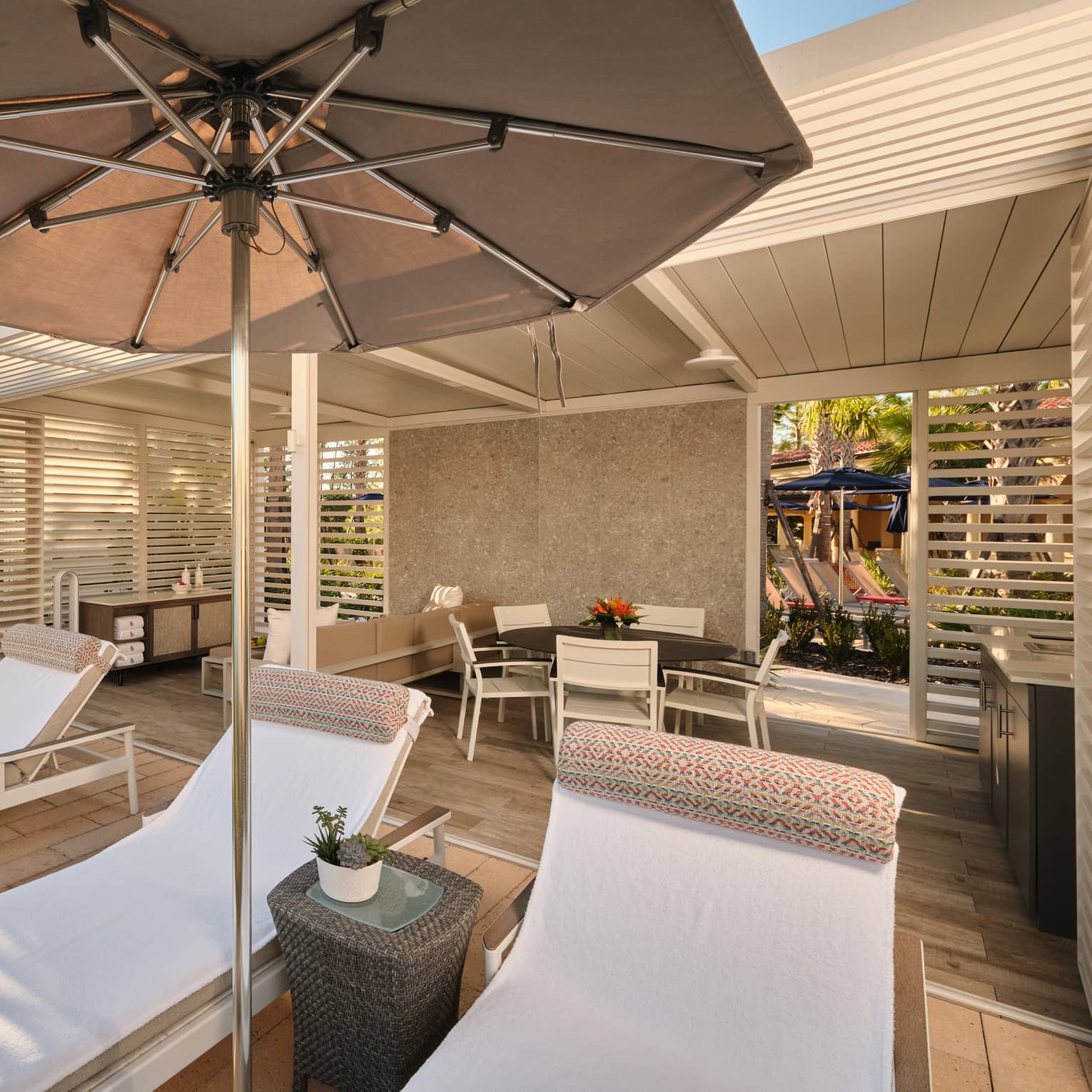 Poolside bungalow with dining table and lounge chairs under an umbrella